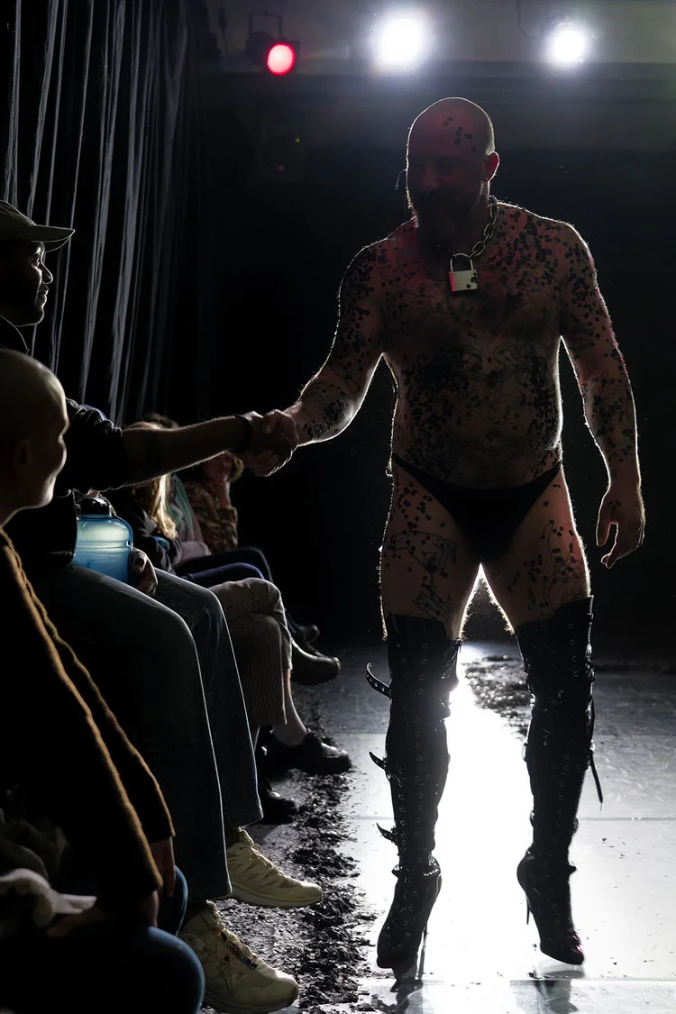 A performer in high boots shakes hands with a seated audience member beside the performance floor.